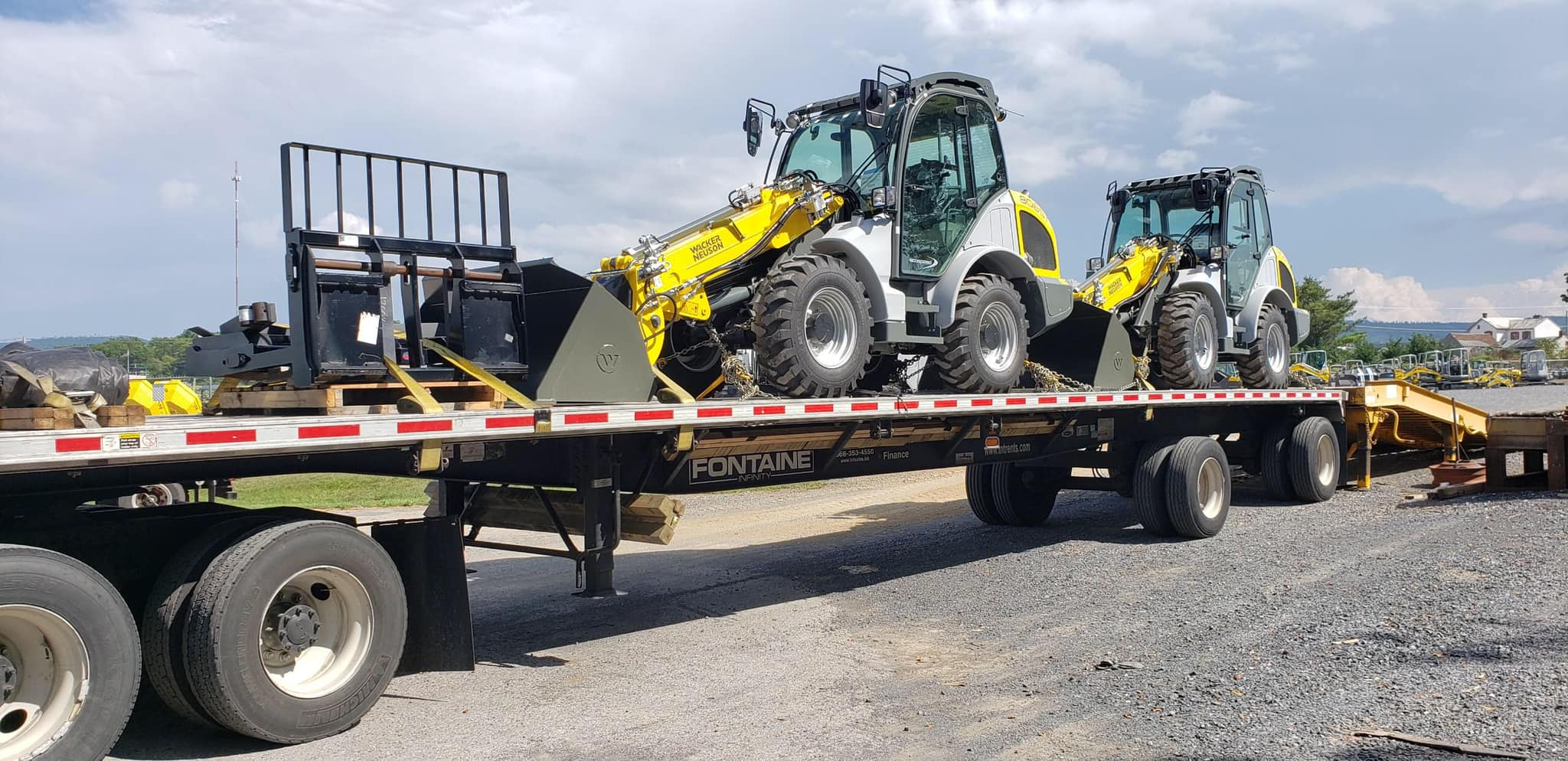 A flatbed trailer transports two yellow and black construction vehicles equipped for excavation work.