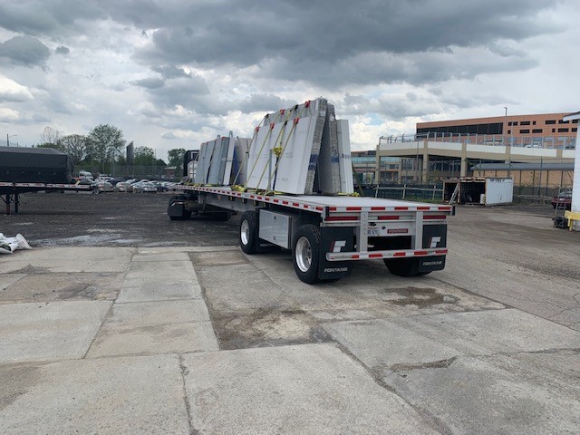 A flatbed truck is loaded with large, rectangular materials and parked in a gravel lot under a cloudy sky.
