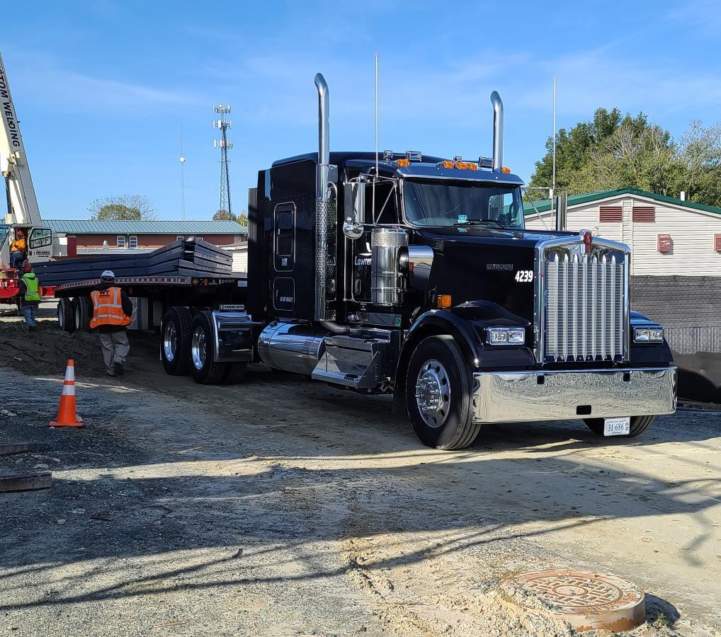 A large black truck with a shiny exterior is parked on a construction site, with workers and equipment visible in the background.